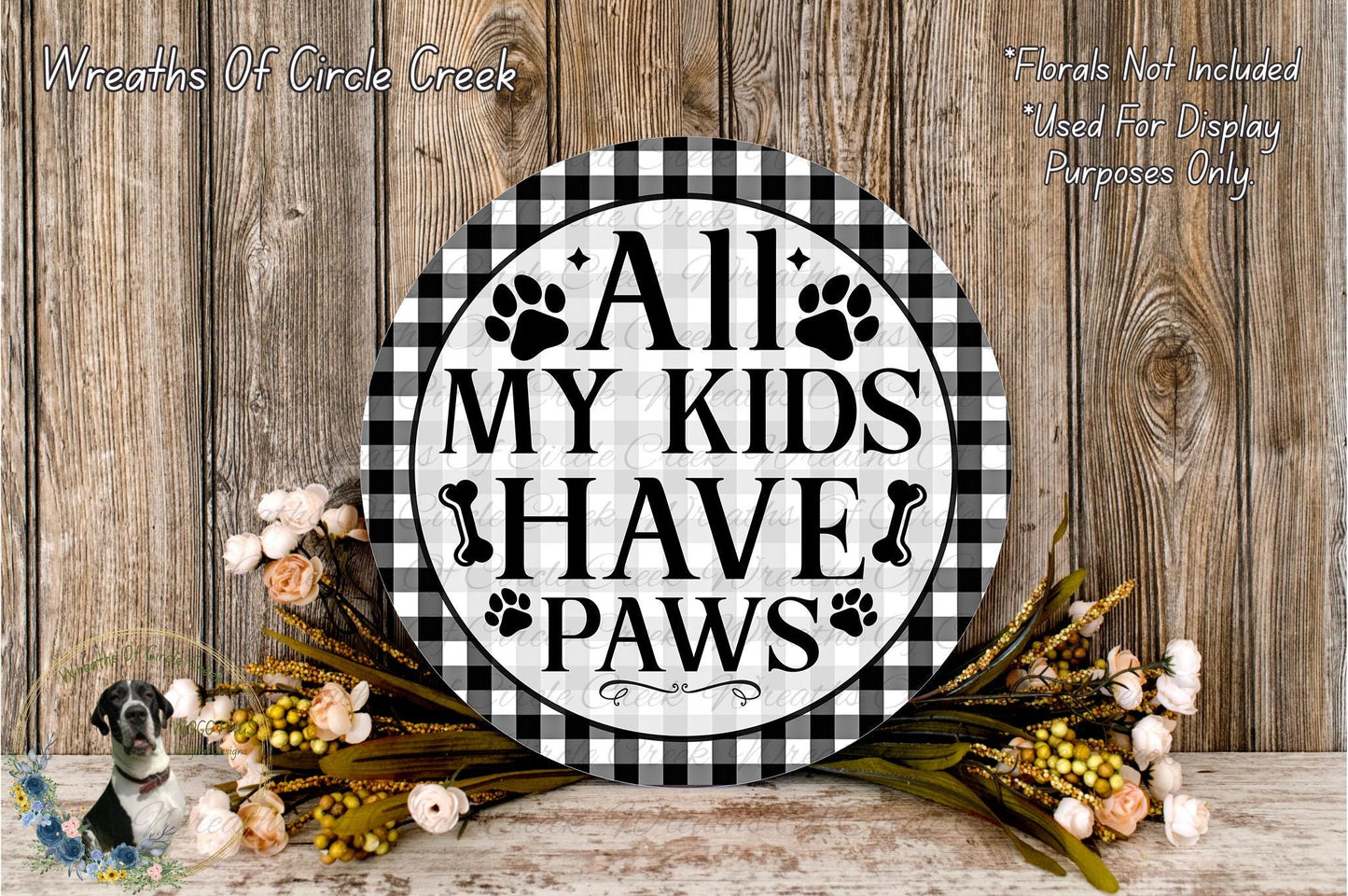 a decorative sign with the text "All My Kids Have Paws" displayed on a wooden surface. The sign is surrounded by a floral arrangement, and there is text in the top left corner that reads "Wreaths Of Circle Creek".