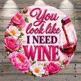 a circular design with a pink background and floral elements surrounding the text "You look like I need wine".
