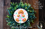 A wreath made of green foliage and featuring a gingerbread man cookie as the centerpiece.