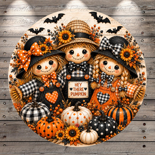 A decorative round wreath featuring three scarecrow dolls, pumpkins, and sunflowers, with the text "Hey there pumpkin" displayed on the wreath.