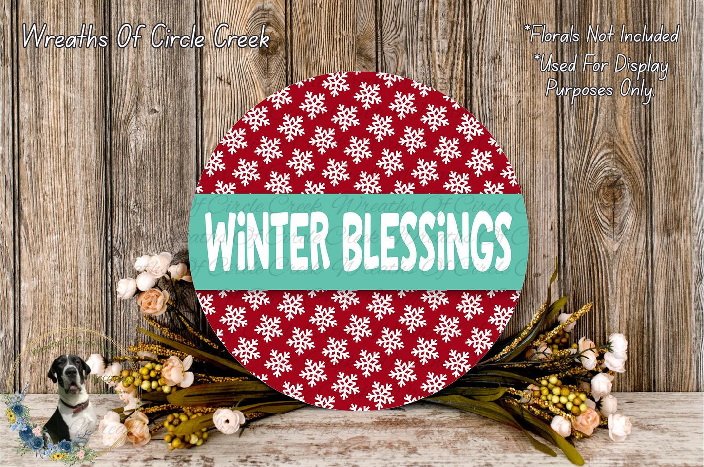 A round wreath with a red and white snowflake pattern, surrounded by a bouquet of flowers, sits on a wooden surface.