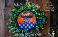 a wreath made of green foliage and a football, with the text "Tallaghties & Touchdowns" written on it. The wreath is displayed on a wooden surface, and there is a small dog in the bottom right corner of the image.