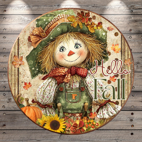 A round, decorative plate featuring a cheerful scarecrow with a hat, scarf, and overalls, surrounded by autumn-themed elements such as leaves, pumpkins, and sunflowers. The plate has the text "Hello Fall" written on it.