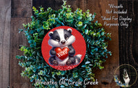 A wreath made of green foliage and a red circular ornament featuring a cartoon badger holding a red heart with the word "XOXO".