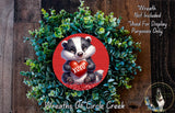 A wreath made of green foliage and a red circular ornament featuring a cartoon badger holding a red heart with the word "XOXO".