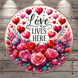 The image is a circular design featuring a floral arrangement with red roses and hearts, surrounded by the text &quot;Love lives here&quot;.