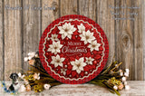 A festive Christmas wreath with white poinsettia flowers and red and white checkered border, placed on a wooden surface. The wreath is surrounded by a variety of flowers and greenery, creating a beautiful holiday display.