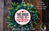 a wreath made of green leaves and a pink sign that reads "This house is full of sweethearts".