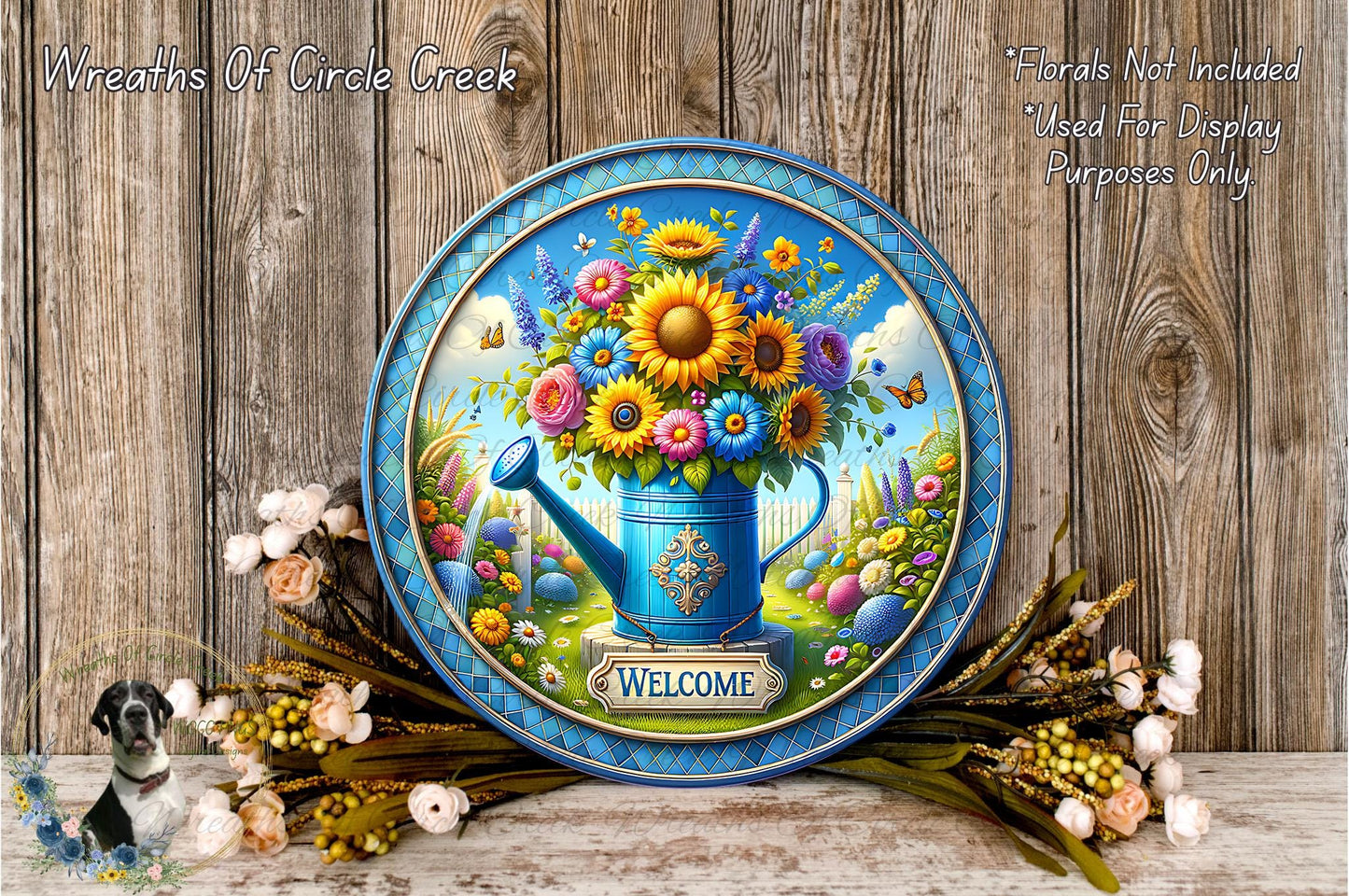 A decorative blue plate with a vibrant floral arrangement and a watering can, surrounded by a wreath of flowers and greenery, against a wooden background.