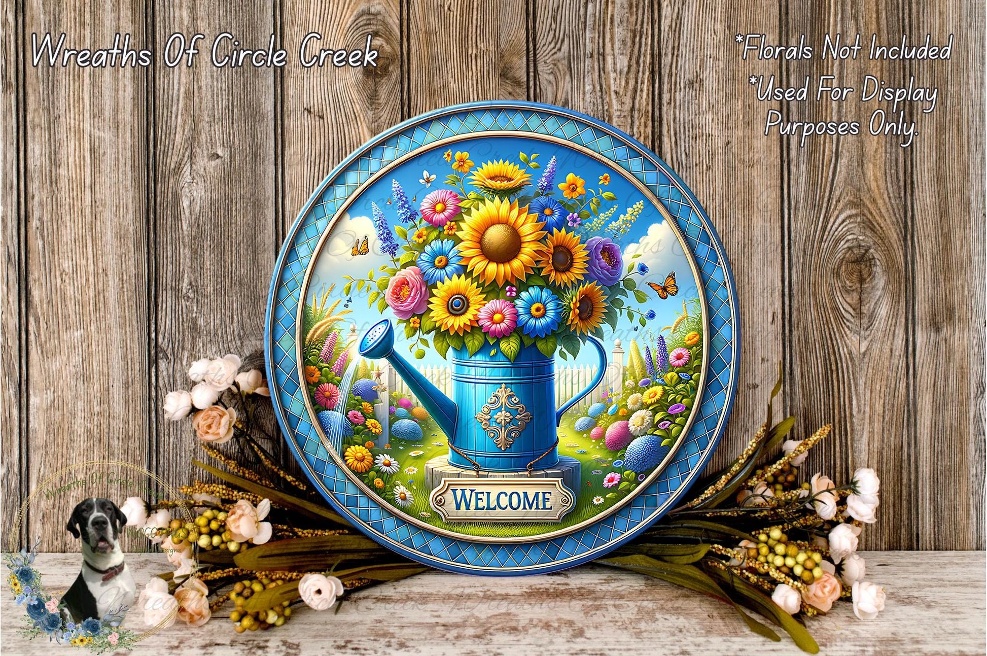 A decorative blue plate with a vibrant floral arrangement and a watering can, surrounded by a wreath of flowers and greenery, against a wooden background.