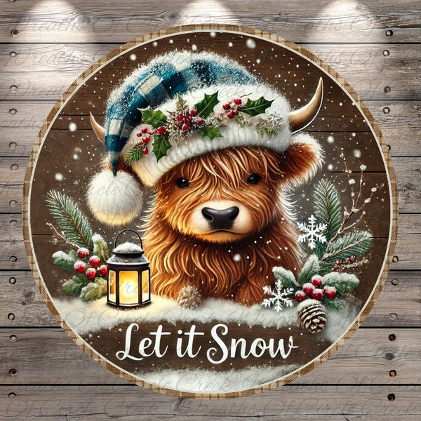 A close-up of a brown cow wearing a blue and white plaid hat with holly leaves and berries, surrounded by snow, pine branches, and a lantern, with the text "Let it Snow" below.