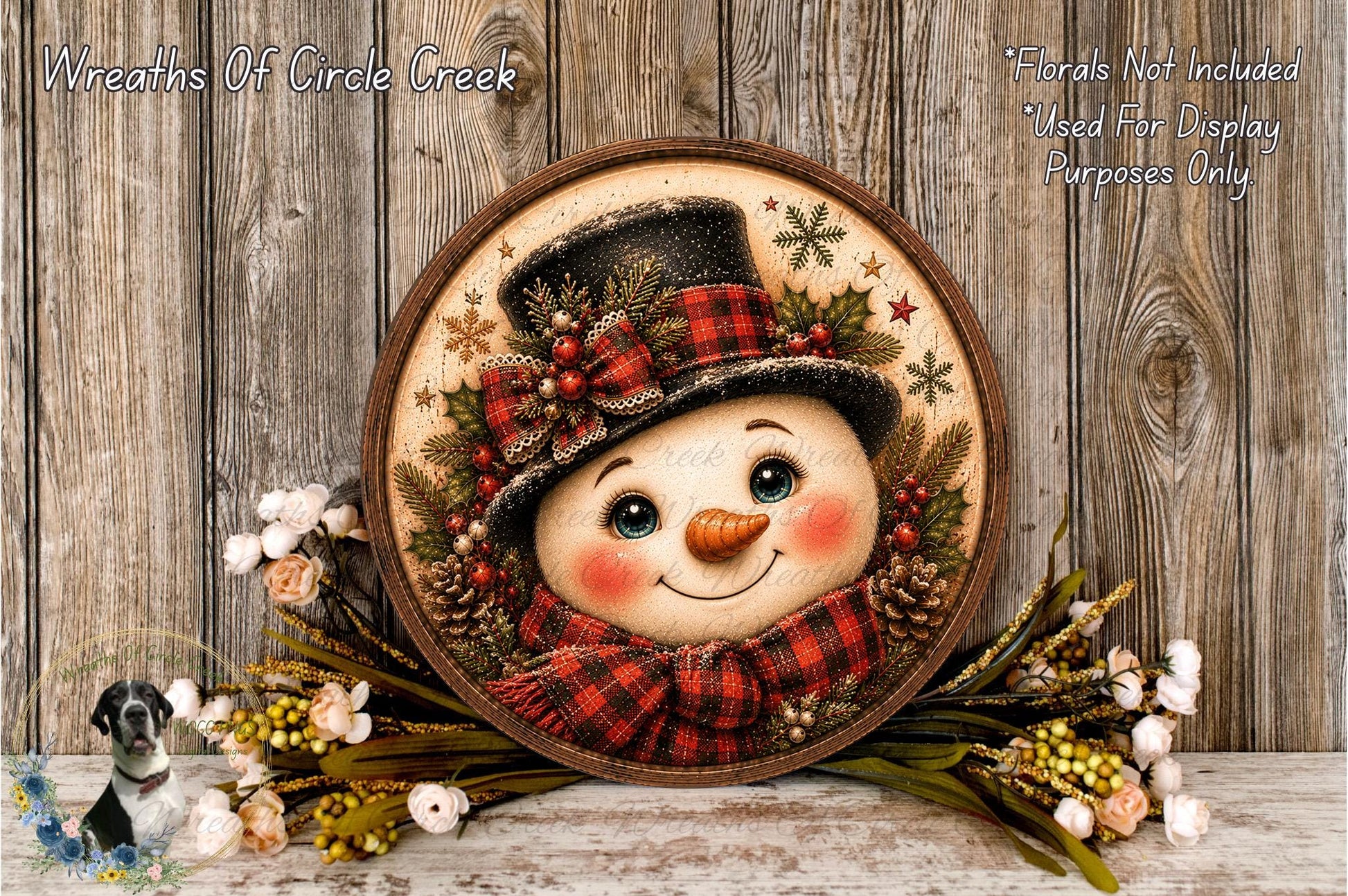 A snowman decoration with a red and black plaid hat, a red scarf, and a carrot nose, surrounded by a wreath of flowers and pine cones, placed on a wooden surface.