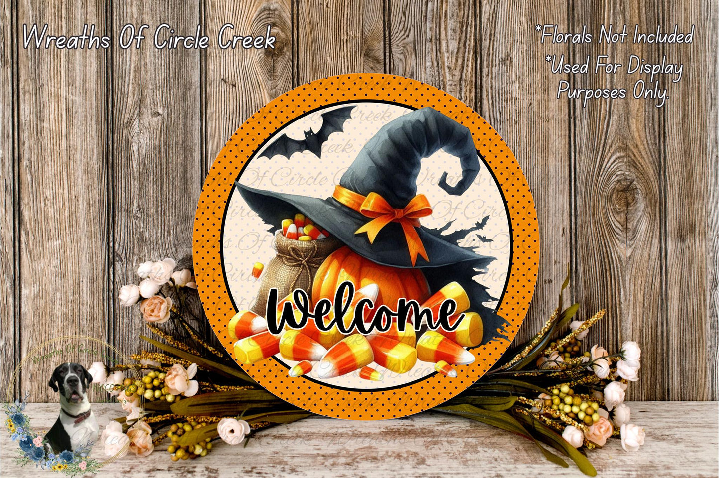 a Halloween-themed wreath with a witch's hat, candy corn, and a "Welcome" sign. The wreath is displayed on a wooden surface, surrounded by flowers and a spooky bat decoration.