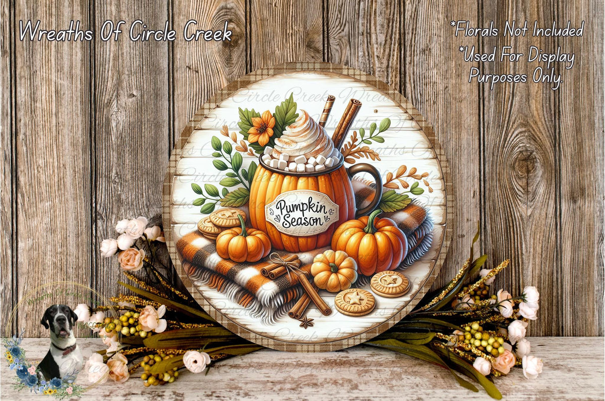 a round wooden plaque with a pumpkin-themed design, surrounded by autumn-themed decorations such as flowers, a scarf, and a mug with a pumpkin.