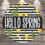 A circular design with a black border and a striped background featuring yellow tulips. The text "Hello Spring" is written in white letters across the center of the design.