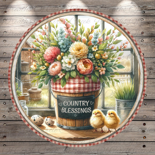 A round wooden frame with a vibrant floral arrangement inside, featuring a bucket with a sign that reads "Country Blessings". Two small chicks are perched on a wooden surface next to the bucket, and there are some eggs and a bird feeder nearby.