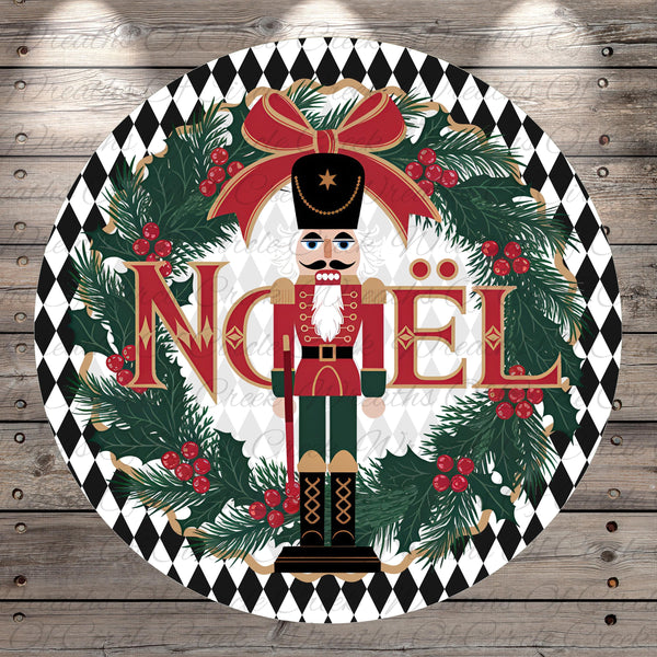 A nutcracker figure surrounded by a wreath of pine branches, berries, and greenery, with the word " Noel" prominently displayed in the center.