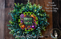 a wreath with the text "TRICK or TREAT" and various Halloween-themed decorations, including pumpkins, bats, and a spider. The wreath is set against a wooden background, and there is a small dog visible in the bottom right corner.