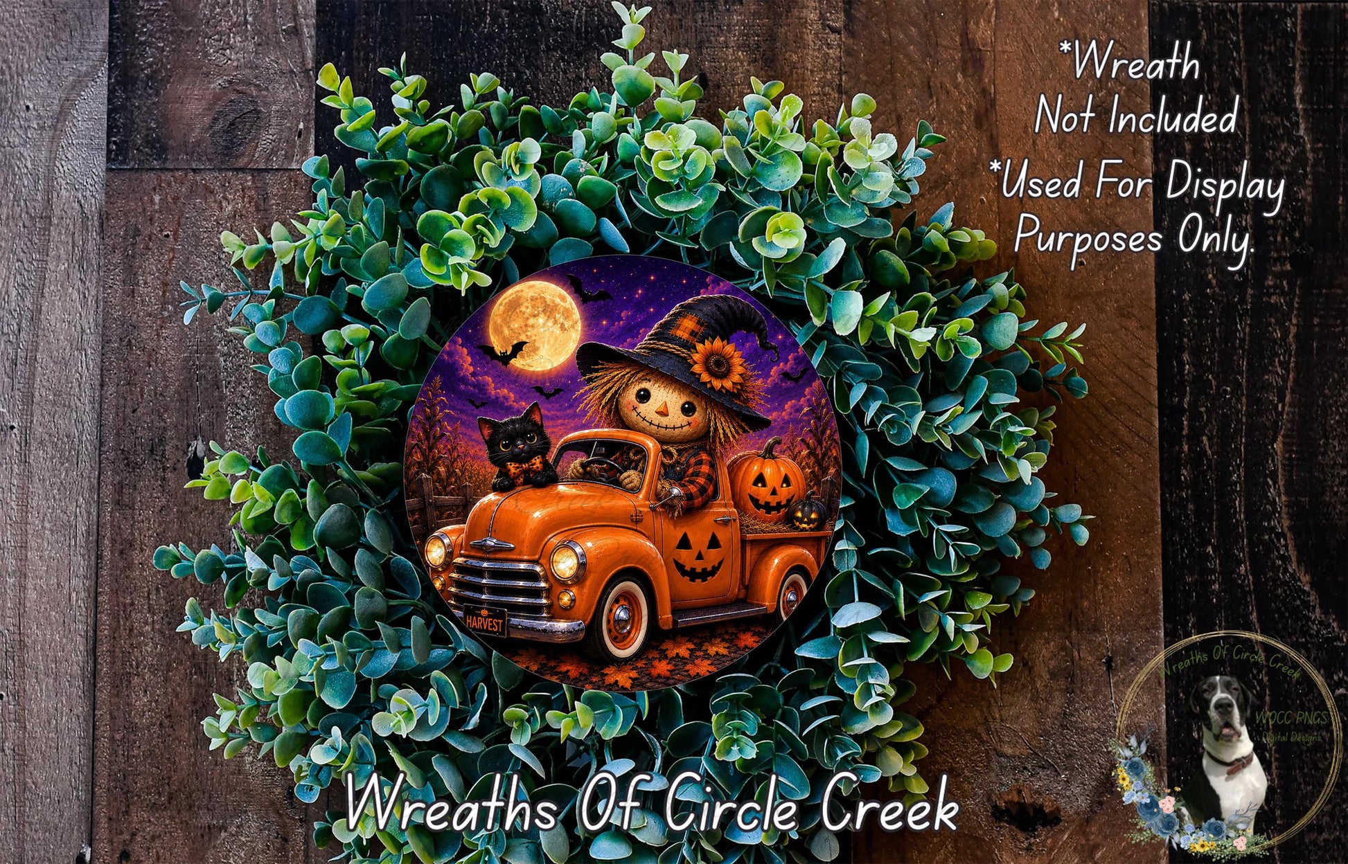A Halloween-themed wreath featuring a scarecrow in a truck, a jack-o-lantern, and a full moon. The wreath is surrounded by greenery and placed on a wooden surface.