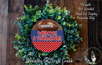 a wreath made of green foliage and a football, with the text "Tailgates & Touchdowns" written on it. The wreath is displayed on a wooden surface, and there is a small dog in the bottom right corner of the image.