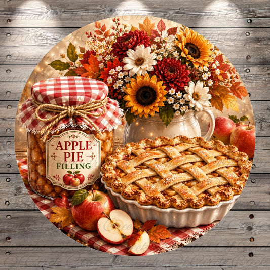 A round wooden table displays a variety of fall-themed items, including a jar of apple pie filling, a vase of sunflowers, apples, and a red and white checkered jar.