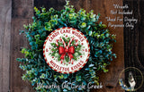 A wreath made of green leaves and red and white ribbons, with a circular sign that says "Candy Cane Wishes Mistletoe Kisses" in the center.