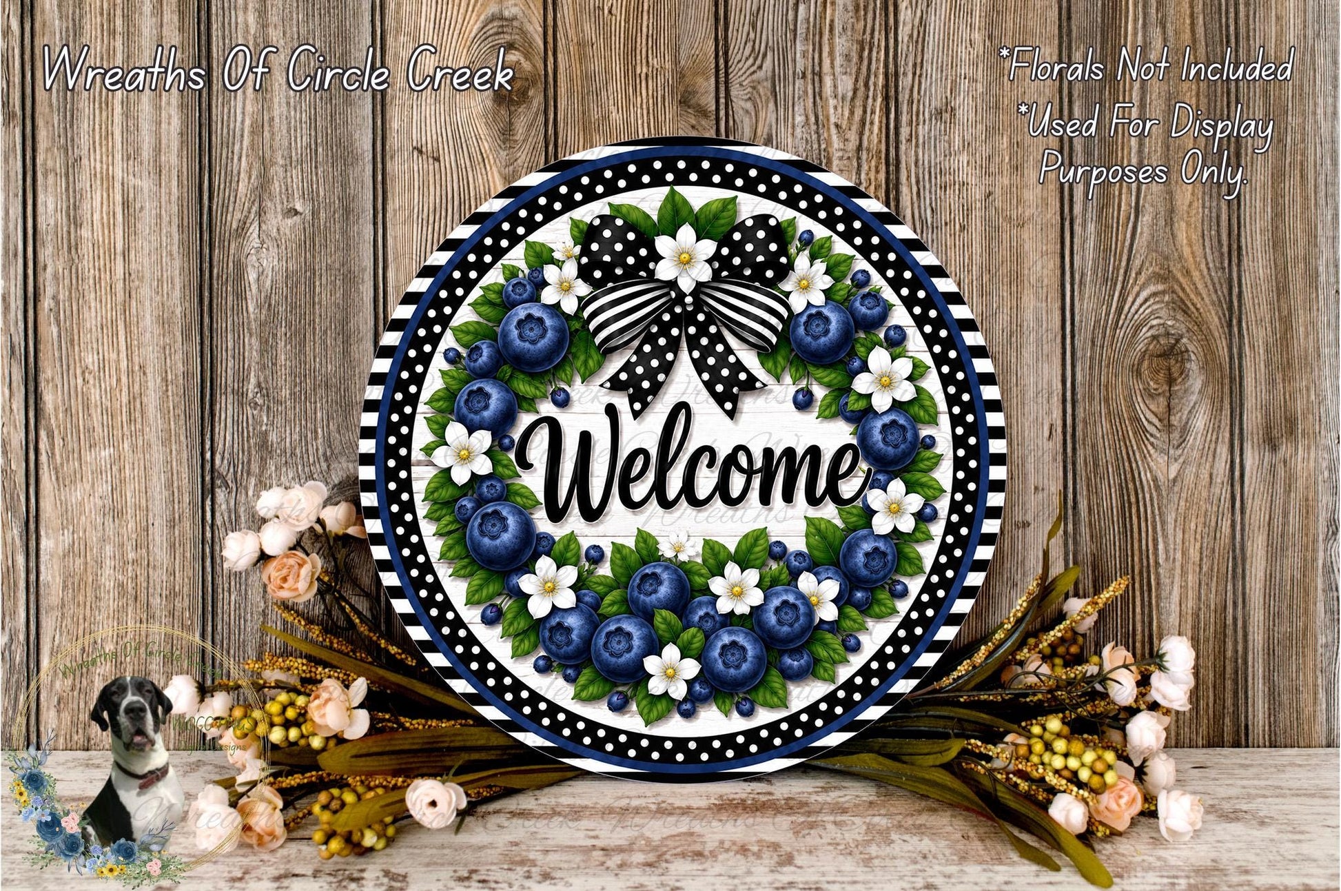 A decorative wreath with the word "Welcome" on it, surrounded by various flowers and foliage, placed on a wooden surface.