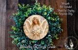 a wreath with a central image of an angel holding flowers, surrounded by a lush green wreath.