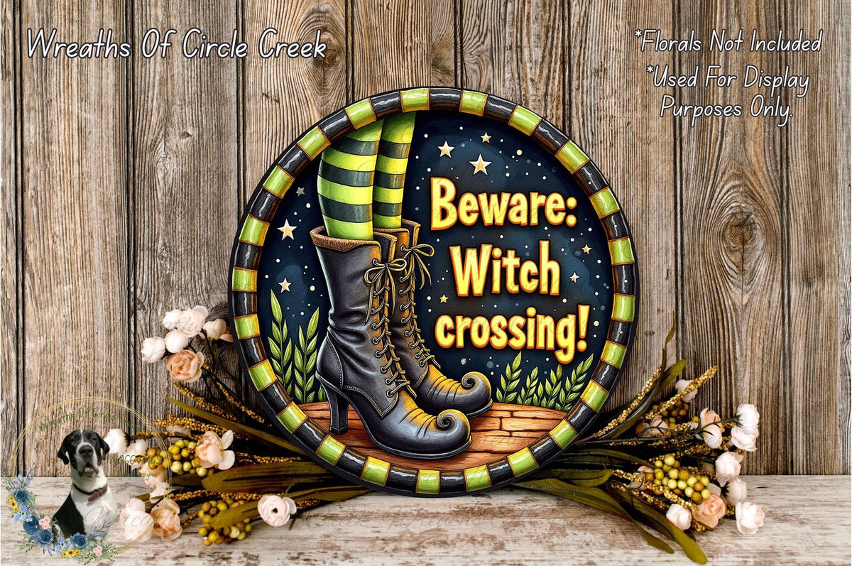 A decorative wreath with a witch's boot and the text "Beware: Witch crossing!" displayed on it, surrounded by flowers and a wooden background.