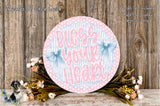 a round sign with the text "Bless your heart" written on it, surrounded by a floral arrangement and a wooden background.