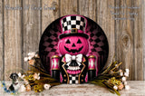 a Halloween-themed wreath with a pumpkin and a nutcracker-like character wearing a top hat and bowtie. The wreath is displayed on a wooden surface, surrounded by flowers.