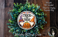 a Halloween-themed wreath made of green foliage and a carved pumpkin, with the text "Trick or Treat" and two gnome-like figures wearing orange hats.