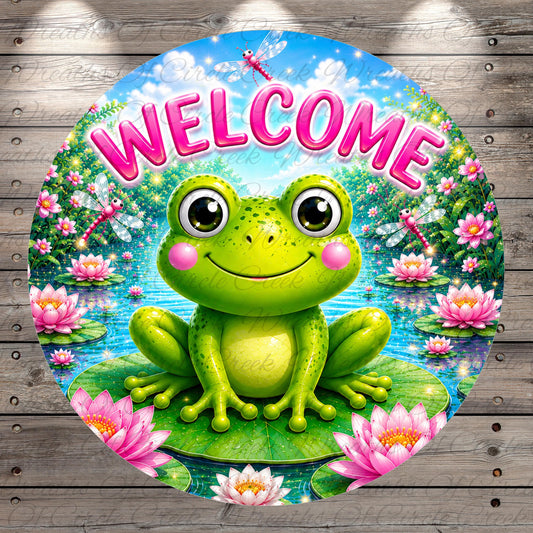 A round, colorful sign featuring a smiling frog sitting on a lily pad surrounded by pink flowers, with a blue sky and fluffy clouds in the background.