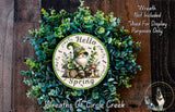A wreath with a gnome and spring-themed design, surrounded by green foliage. The wreath is displayed on a wooden surface.