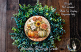 a wreath made of various fall-themed elements, including sunflowers, pumpkins, and greenery, displayed on a wooden surface.