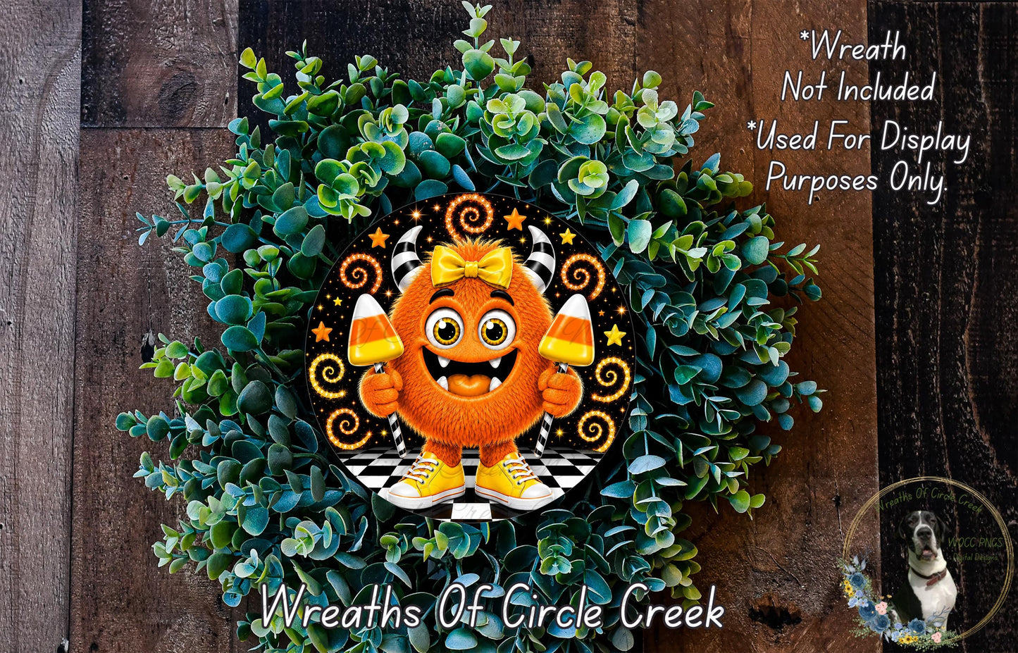 a wreath with a cartoon monster holding candy canes, surrounded by a lush green plant. The wreath is displayed on a wooden surface, and there is a small dog in the bottom right corner of the image.