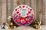 A decorative sign with the text &quot;Love Lives Here&quot; surrounded by a floral arrangement and a wooden background.