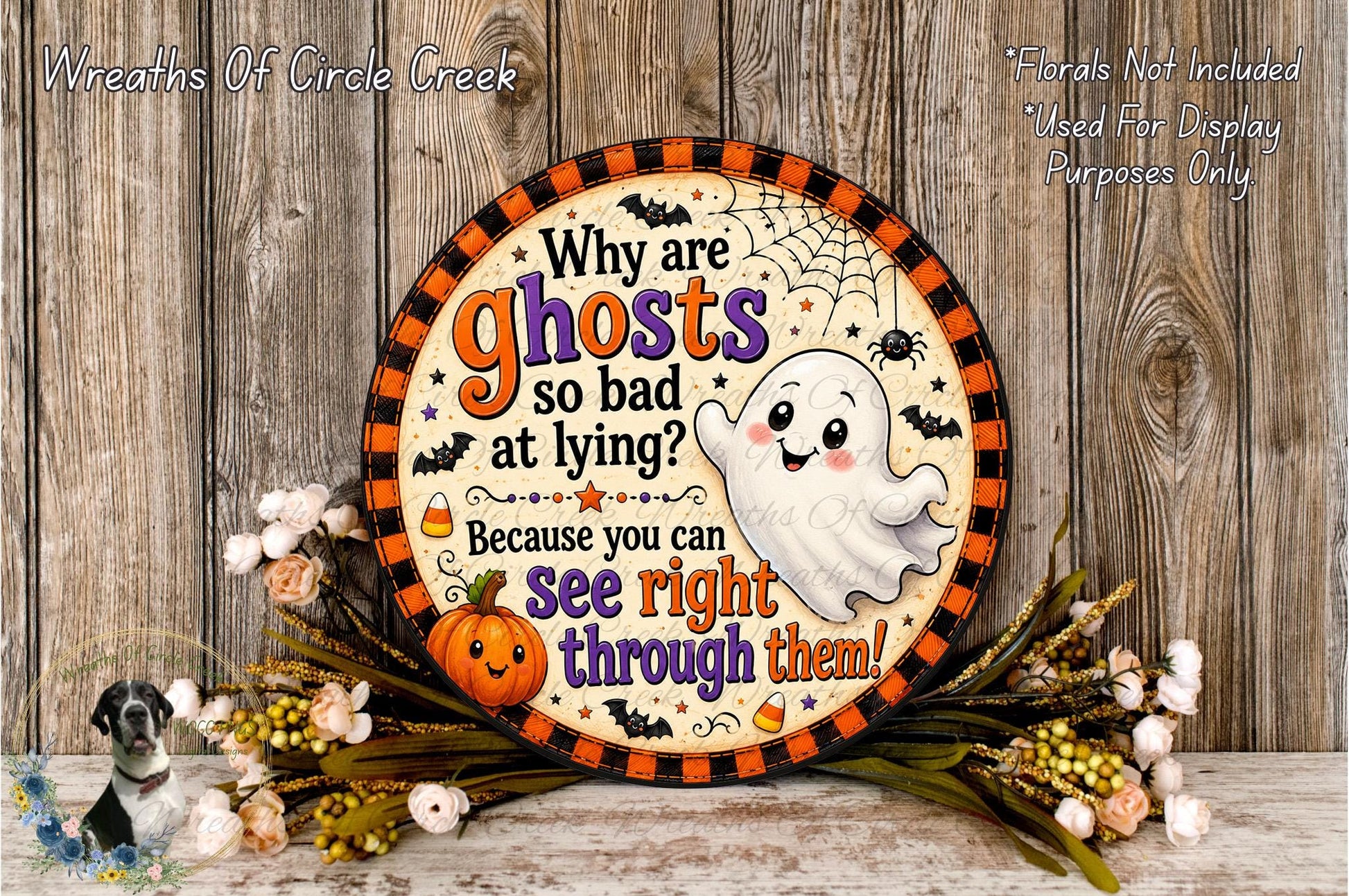 a Halloween-themed sign with a ghost and a pumpkin, surrounded by flowers and placed on a wooden surface.