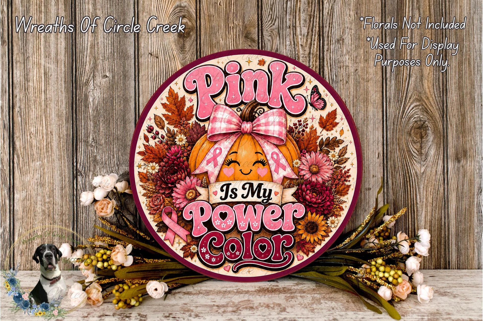 A decorative wreath with a pumpkin and flowers, featuring the text "Is My Power Color" and a pink ribbon symbol, placed on a wooden surface.