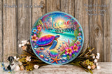 a colorful, circular sign with a turtle and various tropical flowers, placed on a wooden surface. The sign reads "Welcome to our Beach House" and is surrounded by a wreath of flowers.
