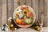 A decorative wreath with a floral design, featuring sunflowers, pumpkins, and other fall-themed elements, is displayed on a wooden surface. The wreath is surrounded by a variety of fall flowers and foliage, creating a festive and seasonal atmosphere.
