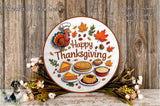 A Thanksgiving-themed wreath with a turkey, autumn leaves, pies, and other fall-themed items, surrounded by flowers and placed on a wooden surface.
