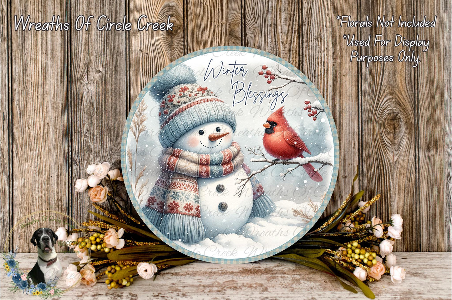 A snowman wearing a scarf and hat stands next to a red cardinal bird on a snowy branch, surrounded by a wreath of flowers and a wooden background.