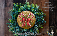 A wreath made of green leaves and red and white candy canes, with a gold bow at the center, is displayed on a wooden surface.