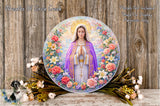 A large, colorful plate featuring a depiction of the Virgin Mary surrounded by a floral wreath. The plate is placed on a wooden surface, with a bouquet of flowers and greenery surrounding it.