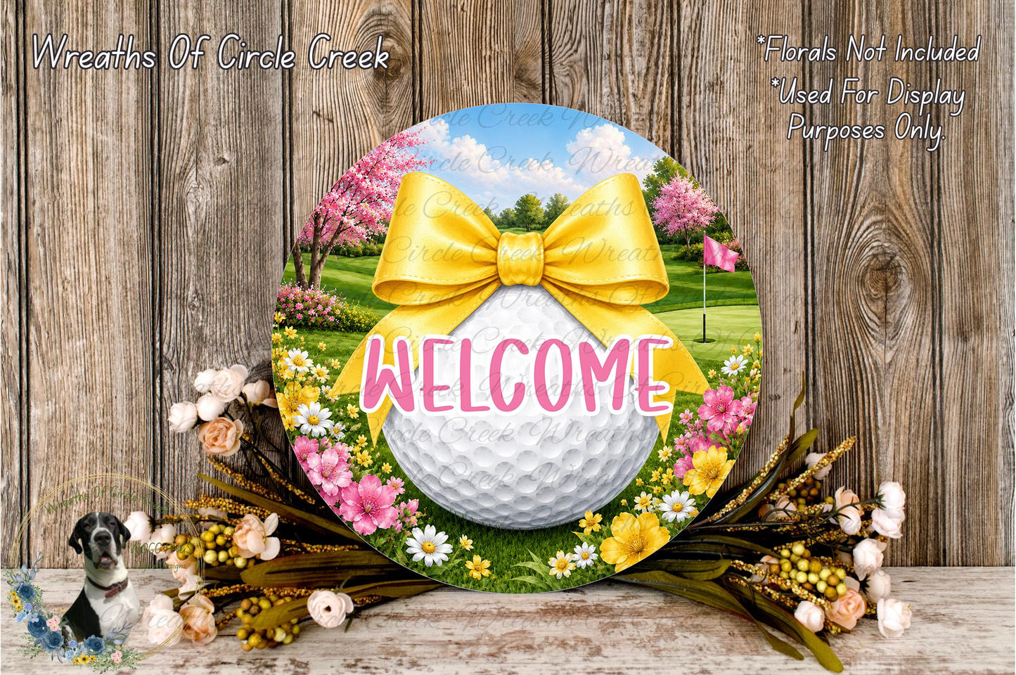 a decorative golf ball-shaped welcome sign with a yellow ribbon and flowers surrounding it, placed on a wooden surface.