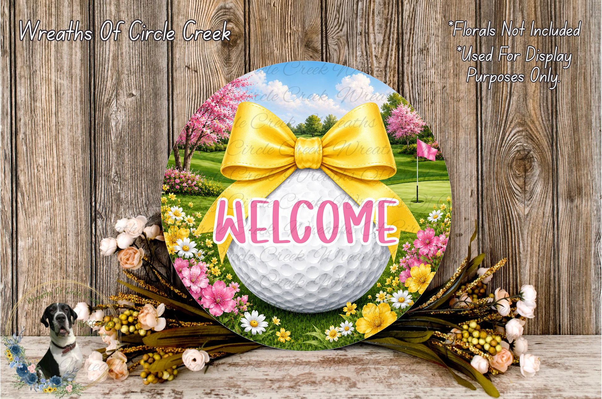 a decorative golf ball-shaped welcome sign with a yellow ribbon and flowers surrounding it, placed on a wooden surface.