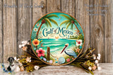 a decorative plate with a tropical beach scene, including palm trees, flowers, and a bird, set against a wooden background.