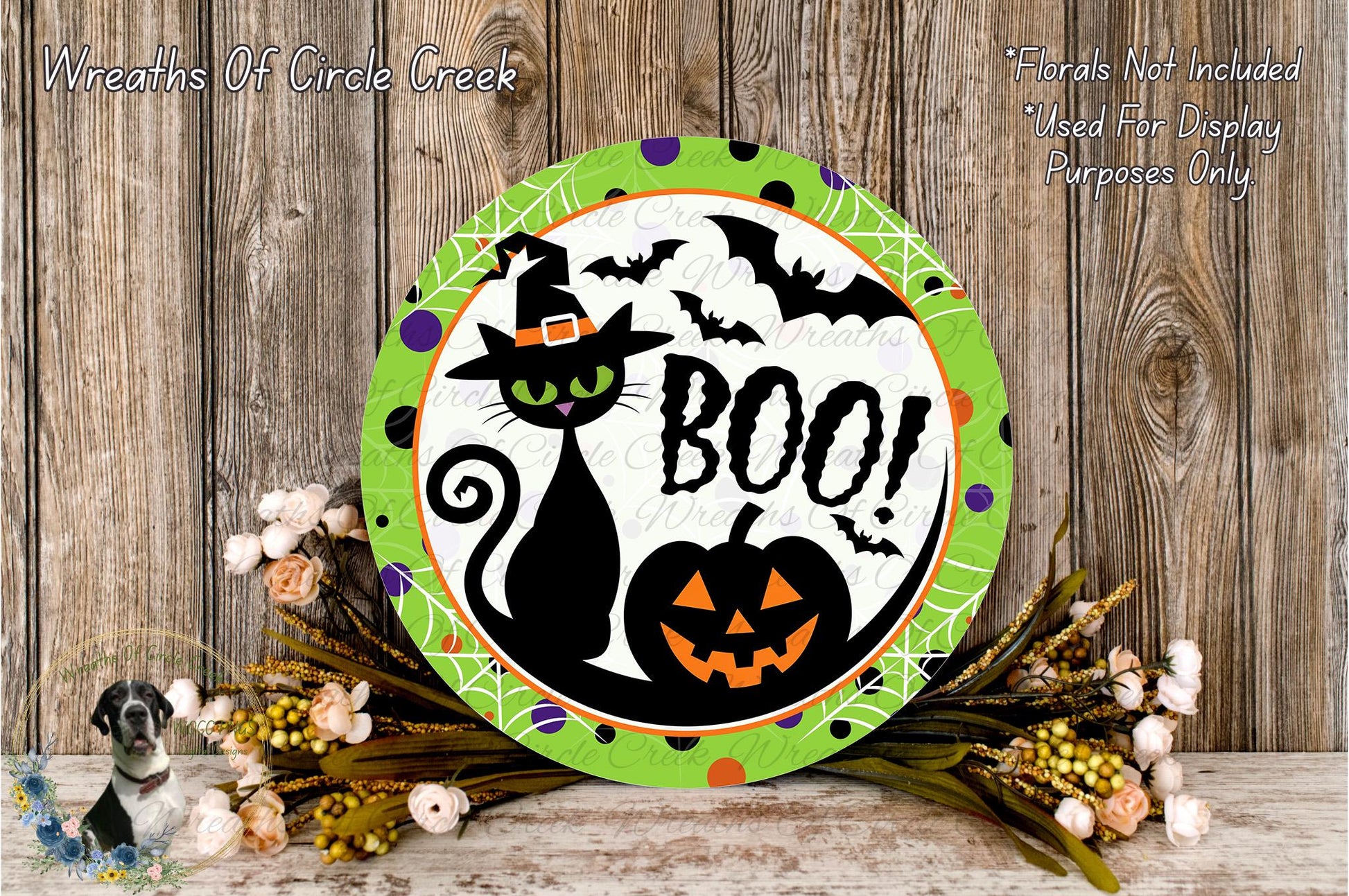 A Halloween-themed wreath with a black cat, a jack-o-lantern, and bats, surrounded by flowers and a wooden background.