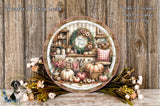 a decorative plate with a wreath and fall-themed items, such as pumpkins, flowers, and a kitchen scene, displayed on a wooden surface.